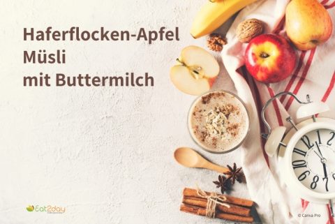 Eine Schale Haferflocken-Apfel-Müsli mit Buttermilch, bestreut mit Haferflocken und Zimt. Daneben liegen ein halbierter Apfel, ein ganzer Apfel, eine Banane, Zimtstangen, Sternanis und ein Wecker auf einem gestreiften Tuch. Links im Bild steht der Titel ‚Haferflocken-Apfel Müsli mit Buttermilch‘.