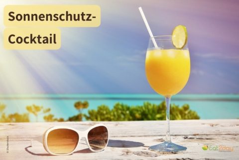 Sonnenschutz-Cocktail: Ein Glas mit orangefarbenem Cocktail und Strohhalm steht am Strand, garniert mit einer Zitronenscheibe. Daneben liegen eine Sonnenbrille und eine halbierte Kokosnuss, im Hintergrund sind Meer und blauer Himmel zu sehen. Oben links steht der Titel ‚Sonnenschutz-Cocktail‘.